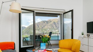 Una sala moderna con un sillón amarillo, un sofá negro y una mesa redonda con un letrero de bienvenida. Un ventanal grande ofrece una vista panorámica de las montañas.