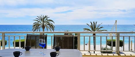 Une terrasse avec une table et des chaises, donnant sur une plage et la mer.