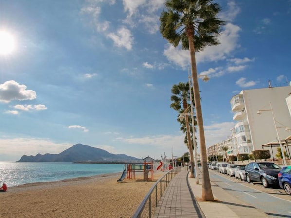 A beach with a playground, palm trees, and a mountain in the background.