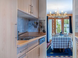 Une cuisine avec des meubles en bois, un évier en acier inoxydable et un coin repas avec une nappe à carreaux.