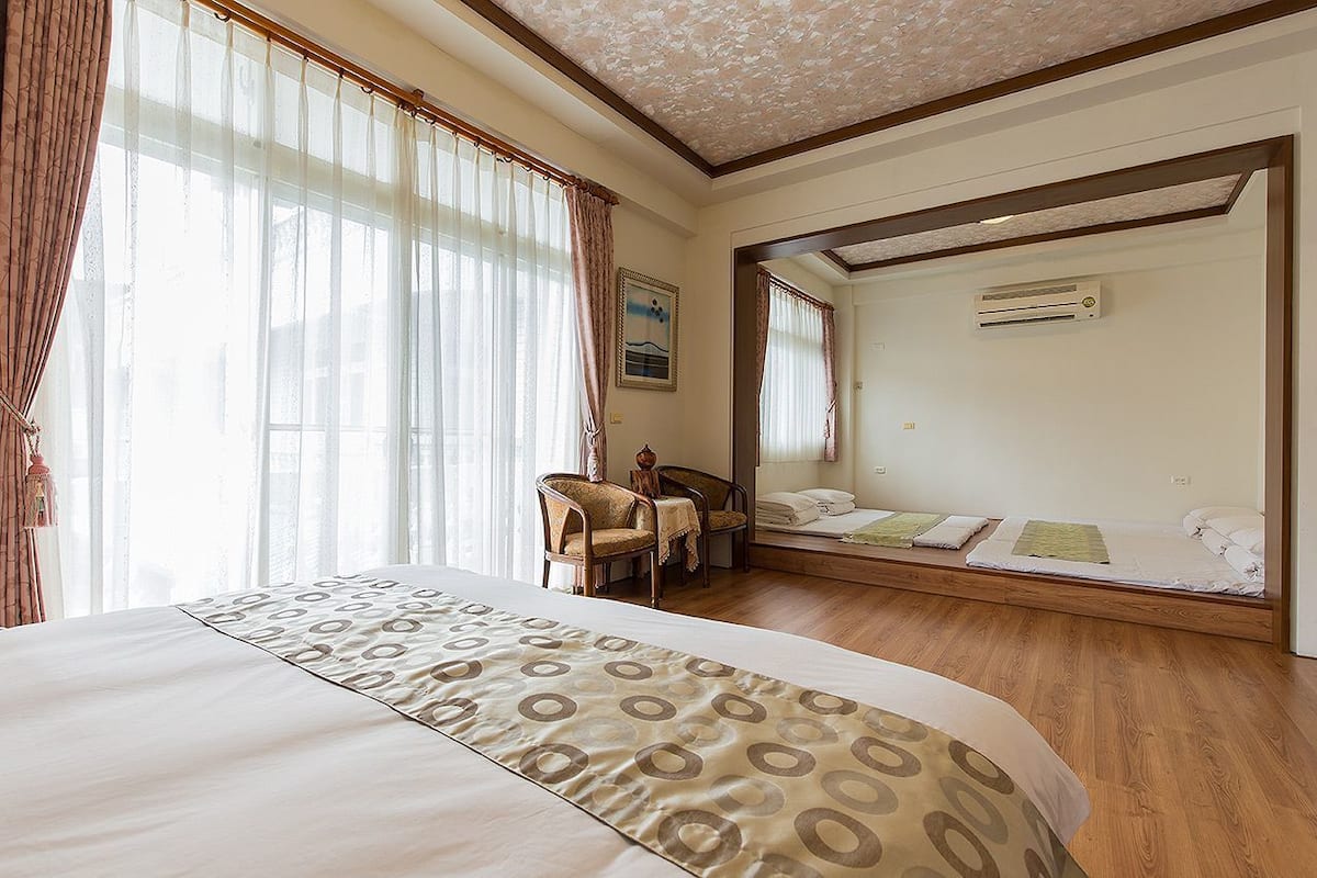 A hotel room with a large bed, a desk, a chair, a small table, and a mirror.