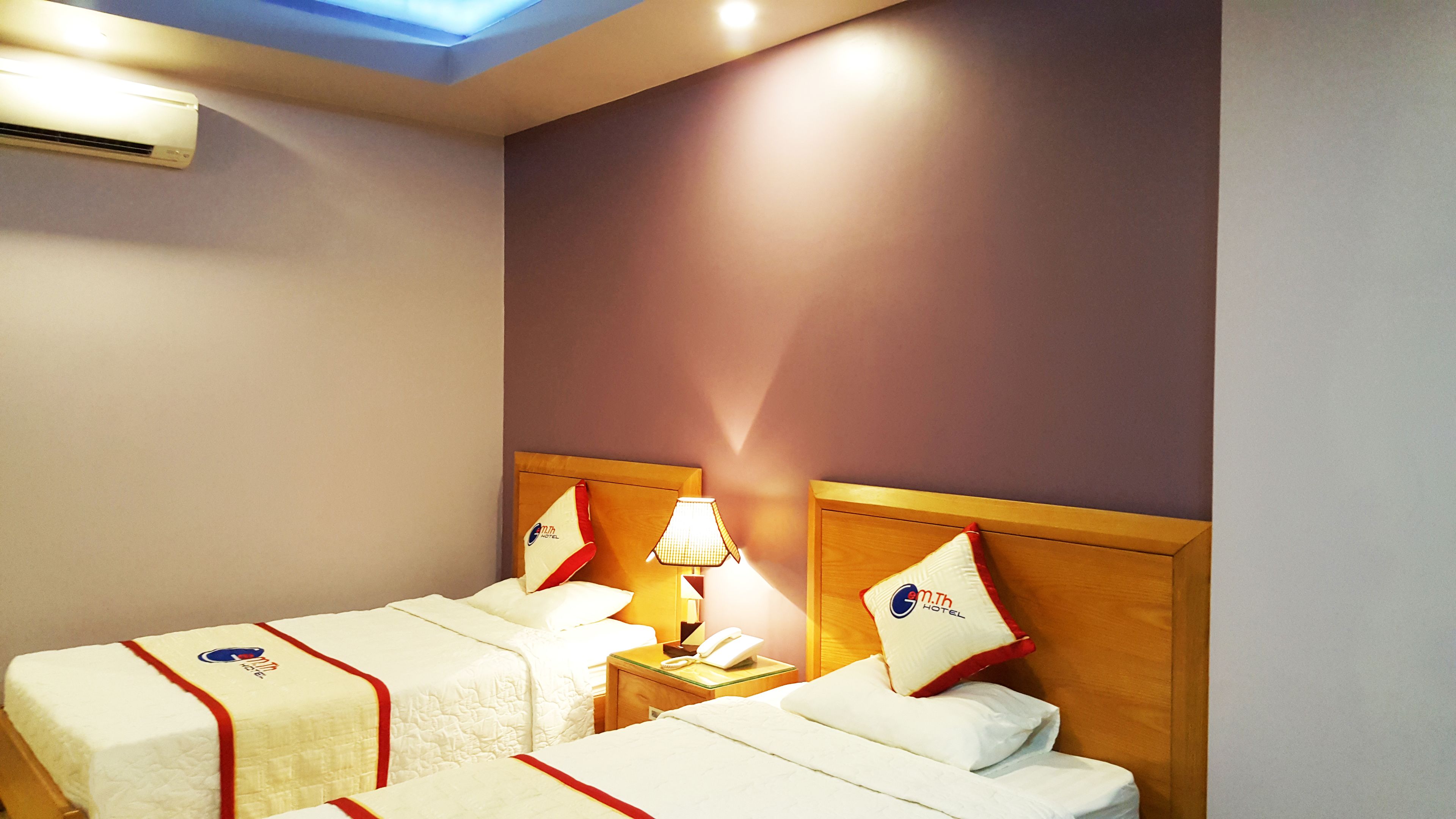 A hotel room with two beds, a nightstand with a lamp, a phone, and a wall-mounted air conditioner.