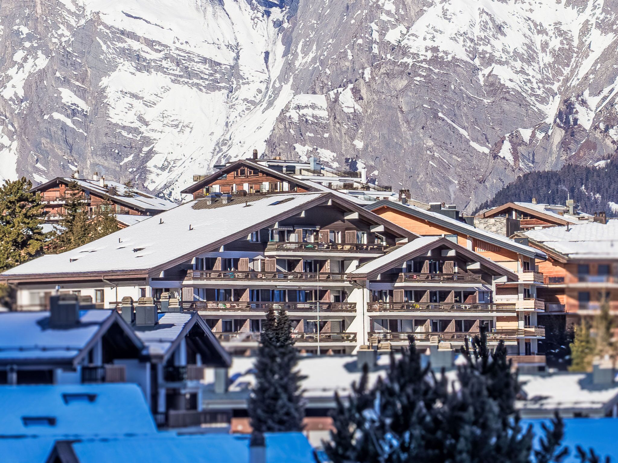 Een meerhoog hotel met een ski-oord op de achtergrond, met balkons en uitzicht op de bergen.