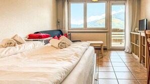 A hotel room with a large bed, a desk, a TV, and a view of the mountains through the window. - Valaisia 35A by Interhome (Nendaz)