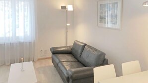 Een moderne woonkamer met een grijze leren bank, een witte tafel en een vloerlamp.