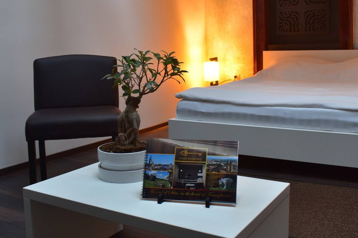 Ein Hotelzimmer mit einem Bett, einem Schreibtisch mit Pflanze, einer Lampe und einem gerahmten Bild an der Wand.