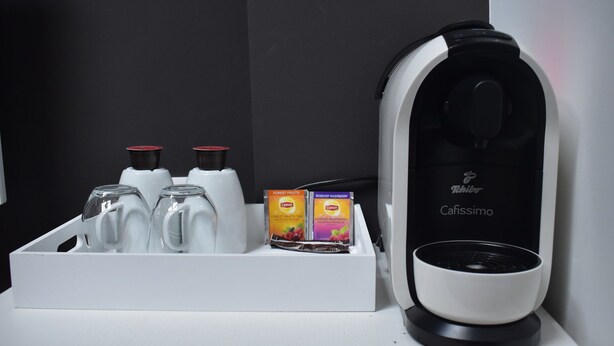 A coffee machine with a cup holder containing two Lipton tea boxes and two Lipton tea bags.