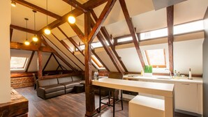 A loft-style room with exposed wooden beams, a long dining table, a sofa, and a kitchen area with a sink and countertop. - Vendi Grand Square Residence (Sibiu)