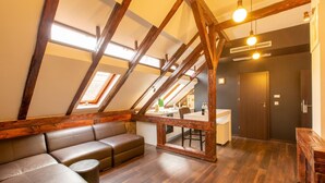 A loft-style room with a sloped ceiling, wooden beams, a sofa, a dining table, and a kitchen area. - Vendi Grand Square Residence (Sibiu)
