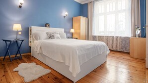 Een slaapkamer met een bed, twee nachtkastjes, een raam met gordijnen en een wollen vloerkleed op de houten vloer.