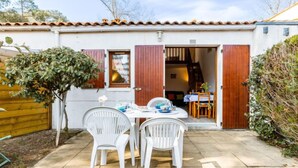 Una casa pequeña con un patio, una mesa de comedor con sillas y una valla de madera.