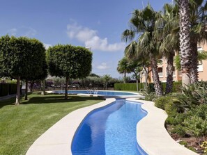 A swimming pool with a curved design, surrounded by well-maintained grass and palm trees.