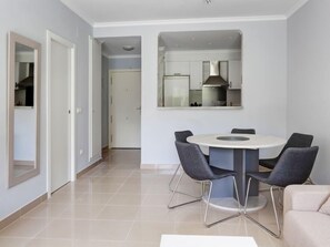 A modern dining area with a round table and four chairs, a sofa, and a kitchen visible through an open door.