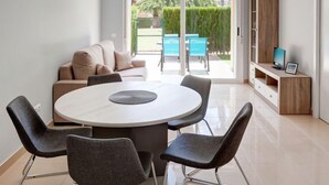 Una sala de estar moderna con una mesa de comedor redonda, sillas grises, un sofá beige y un televisor sobre un mueble de madera.