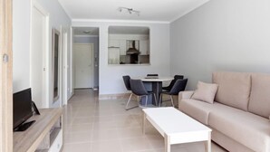 Una sala de estar moderna con un sofá color beige, una mesa de centro blanca y un comedor con una mesa pequeña y sillas.