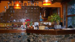 Zona de bar con paredes de piedra, mostrador de madera, estantes con diversos objetos y luces colgantes.