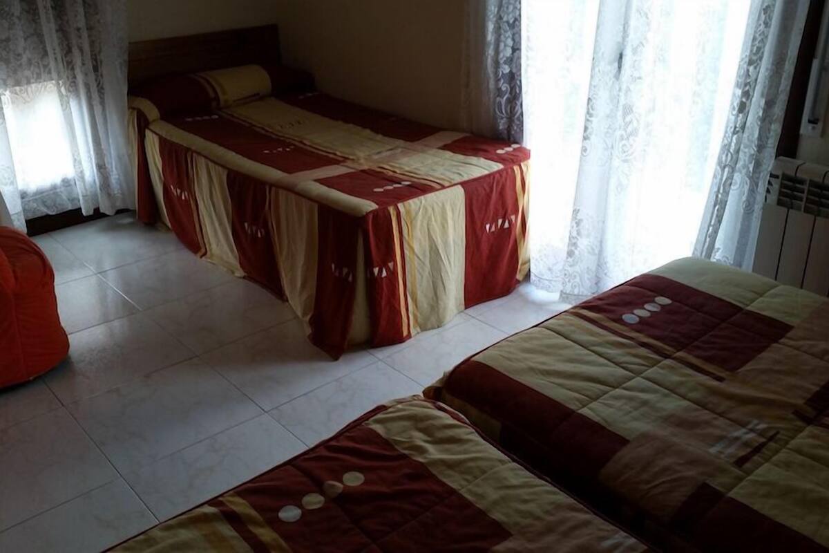 A bedroom with two beds, a red bean bag chair, and a window with curtains.
