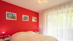 Quarto com parede vermelha, cama branca e três quadros emoldurados.