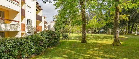 Een woonwijk met een verzorgd gazon, volwassen bomen en een rij moderne appartementen met balkons.