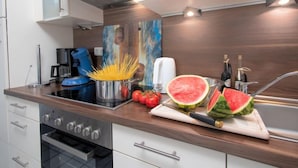 Een moderne keuken met witte kasten, een roestvrijstalen fornuis, een koffieapparaat en verse tomaten en watermeloen op het aanrecht.
