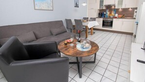 Een moderne woonkamer met een grijze bank, een ronde houten salontafel en een eethoek met een witte tafelkleed.