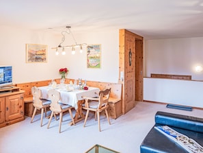 A cozy dining area with a wooden table set for four, surrounded by wooden chairs. There is a wooden cabinet to the left and a blue sofa with a map on it to the right.