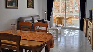 A living room with a sofa, a dining table with chairs, a TV, and a sliding glass door leading to an outdoor area with chairs. - Celio I by Interhome (Albir)