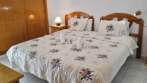 A double bed with floral bedding, a wooden headboard, a bedside table with a lamp, and a wooden wardrobe. - Celio I by Interhome (Albir)