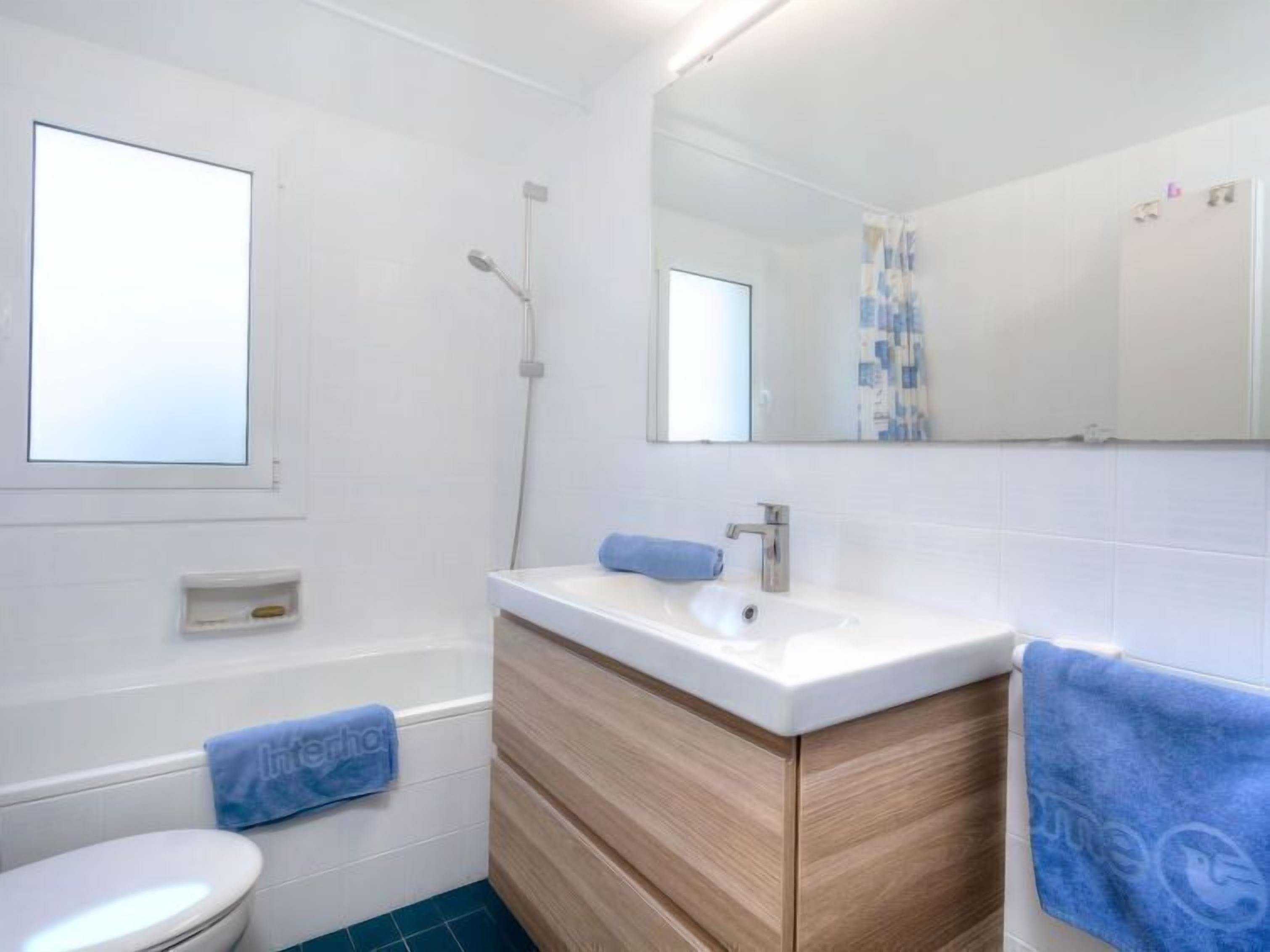 Een moderne badkamer met een wit wastafelmeubel, houten opbergkast en een blauwe handdoek.