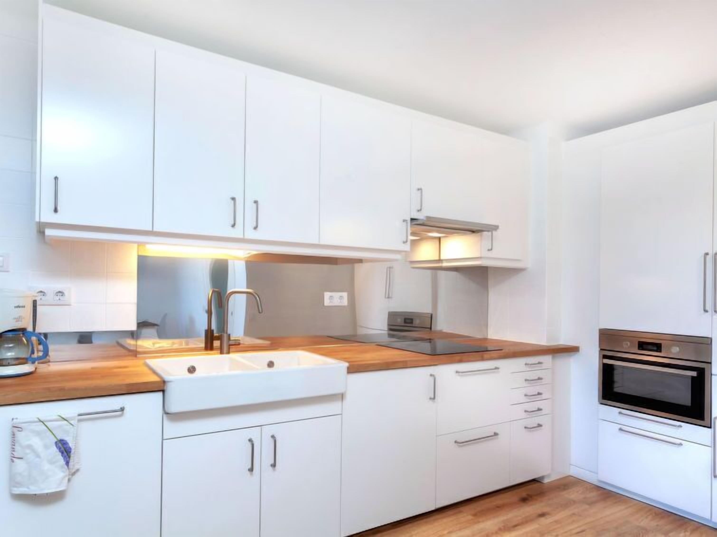 A modern kitchen with white cabinets, a wooden countertop, a stainless steel sink, and a built-in oven.
