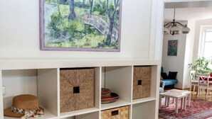 Ein Wohnzimmer mit einem weißen Bücherregal, einem Gemälde einer Brücke, einer Chandelierleuchtre und einem roten Teppich.