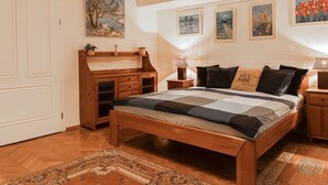 Ein Schlafzimmer mit einem hölzernen Bett, einem Nachttisch, einer Holzkommode und einem großen Fenster.