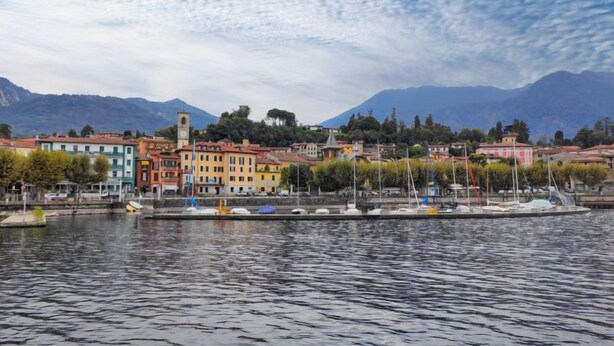 A waterfront view with colorful buildings, a dock with boats, and mountains in the background.