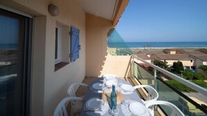 A balcony with a table set for dining, overlooking a beach and ocean.