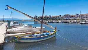 A marina with boats docked, a wooden pier, and buildings in the background.