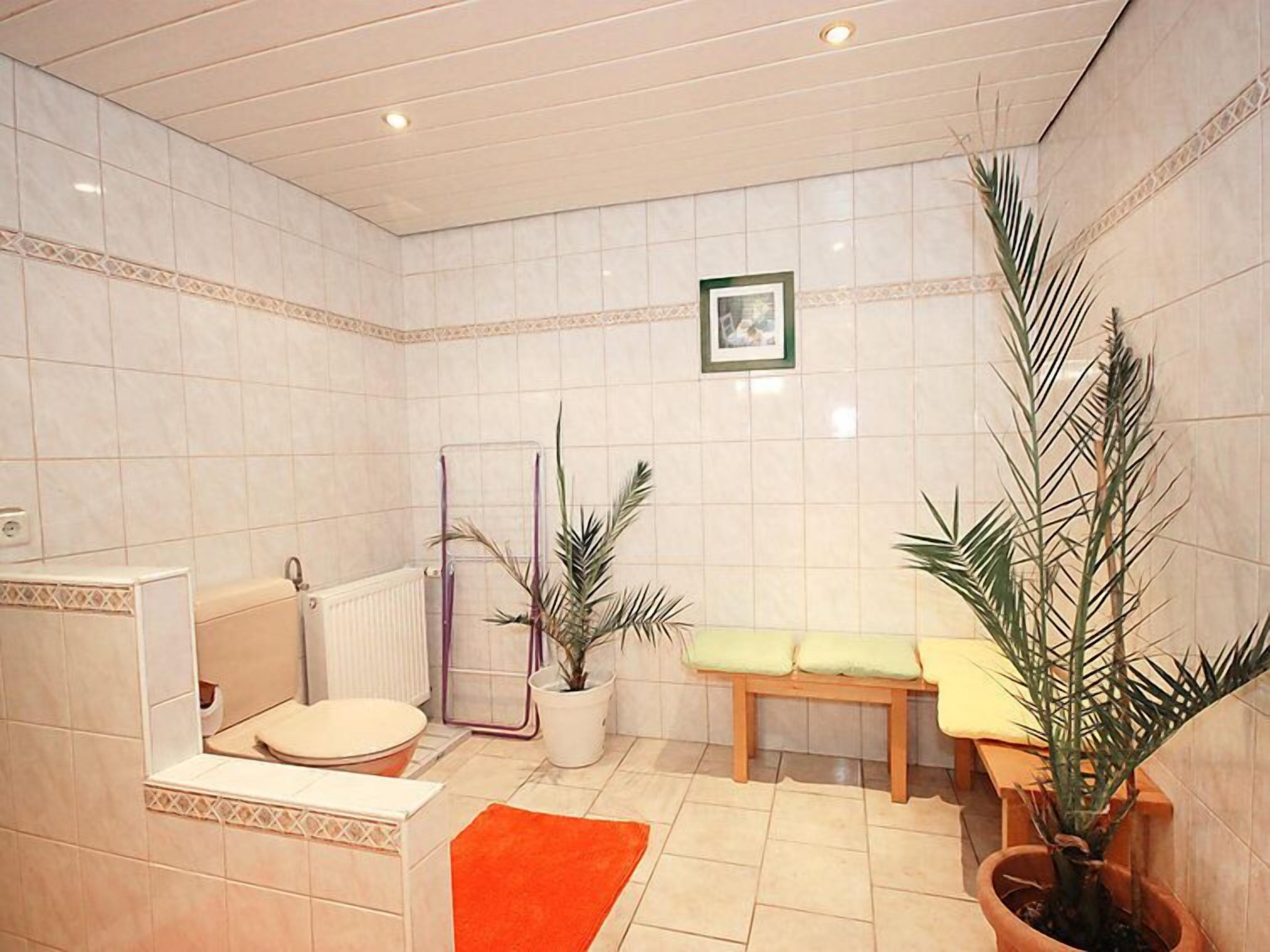 Une salle de bain avec une baignoire, des toilettes, un banc et des plantes en pot.