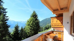 Un balcón con mesa y sillas de madera, con vistas a un paisaje montañoso.