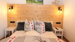 Un dormitorio con cabecera de madera, dos mesitas de noche, una cama con almohadones decorativos y un cuadro de un paisaje montañoso sobre la cabecera.