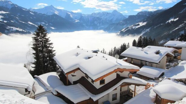 Un pueblo cubierto de nieve con edificios de estilo chalet, cielo despejado y vistas a montañas distantes.