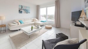 A modern living room with a white sofa, a coffee table, and a TV on a stand.