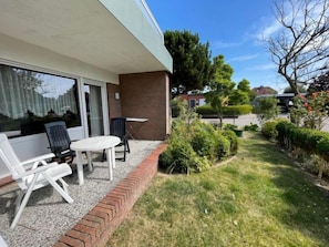 Enjoy a peaceful outdoor space with a patio featuring a table and chairs, surrounded by lush greenery and a charming brick building.
