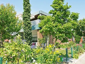 Residential building with a flat roof and balcony, set amidst a lush garden.