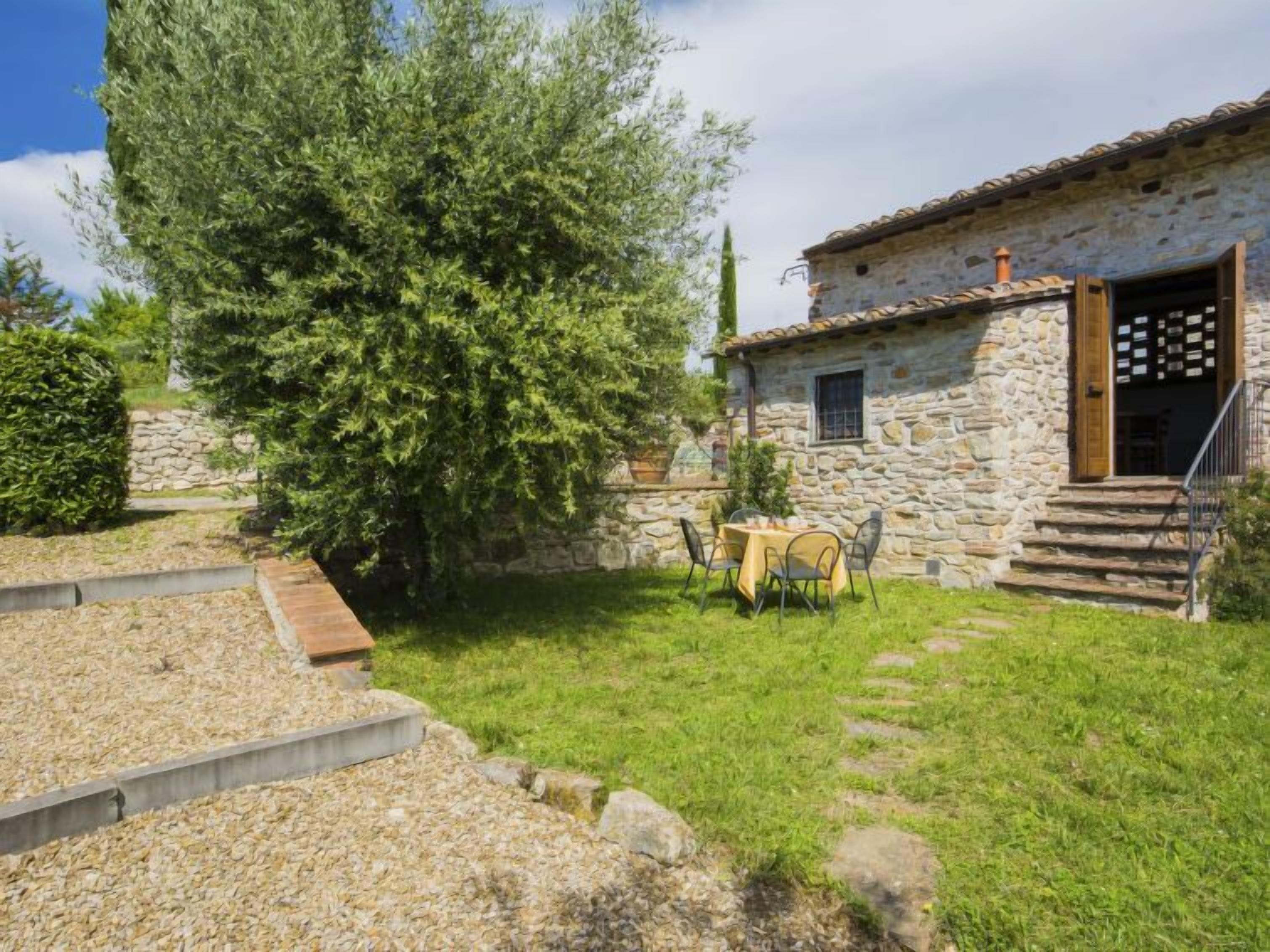 A stone house with a garden, a table with chairs, and a staircase leading to the entrance.