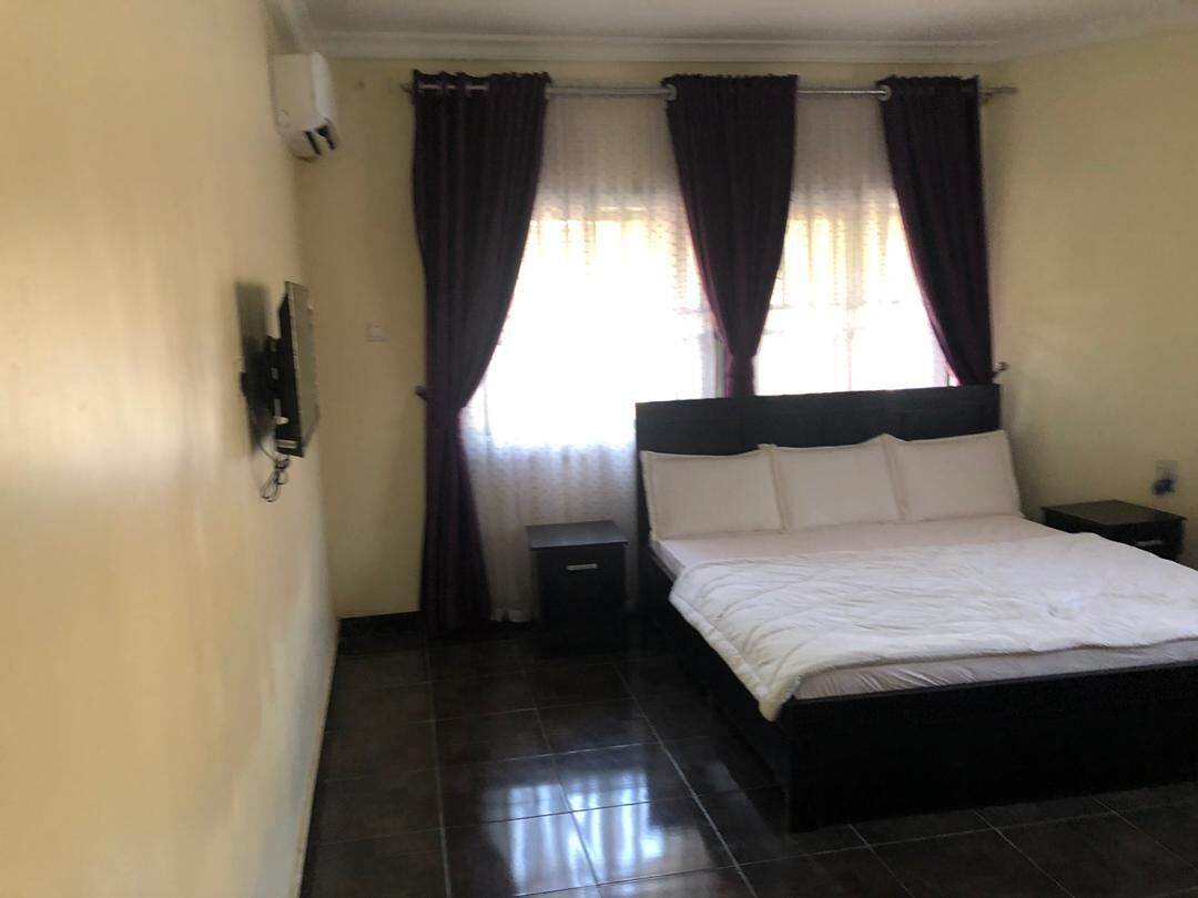 A bedroom with a bed, a nightstand, a wall-mounted phone, and a window with curtains.