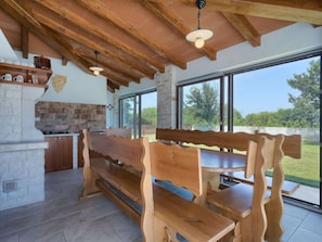 A rustic kitchen with a stone wall, wooden bench seating, and large windows offering a view of the outdoors. - Mirjana by Interhome (Barban)