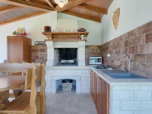 A kitchen with a stone fireplace, wooden cabinets, and a built-in microwave. - Mirjana by Interhome (Barban)