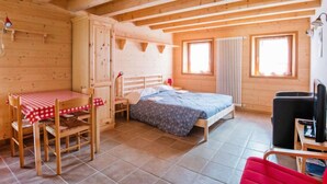 A wooden cabin with a bed, a table with chairs, and a television. - Albergo Diffuso - Cjasa de Barce by Interhome (Barcis Lake)