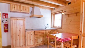 A wooden cabin with a kitchen area, including cabinets, a table with chairs, and a fire extinguisher. - Albergo Diffuso - Cjasa de Barce by Interhome (Barcis Lake)