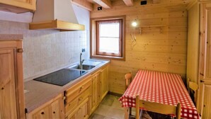 A compact kitchen with wooden cabinets, a window, and a table with a checkered tablecloth. - Albergo Diffuso - Cjasa de Barce by Interhome (Barcis Lake)