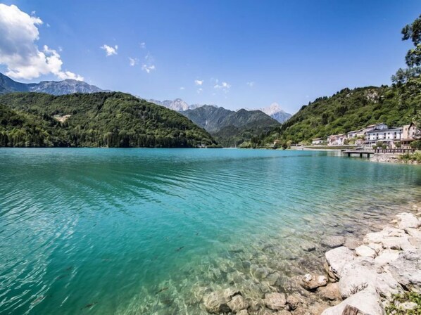 A clear lake with a rocky shoreline, surrounded by lush green hills and mountains. - Albergo Diffuso - Cjasa de Barce by Interhome (Barcis Lake)